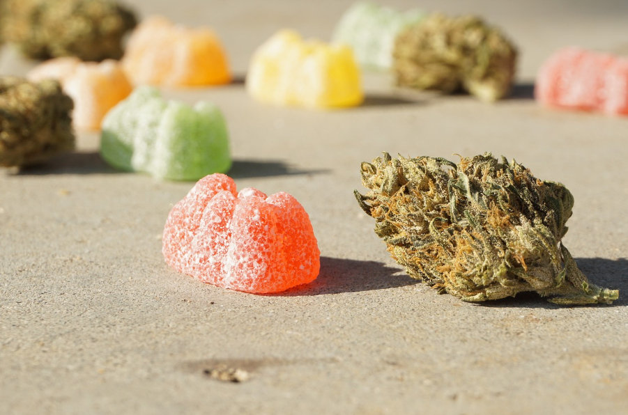 Close up of an orange gummy next to a weed flower. Other flowers and gummies are in the background