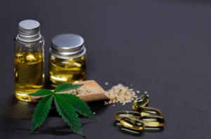 Two small jars of oil, a marijuana leaf, and gel caps against a black background